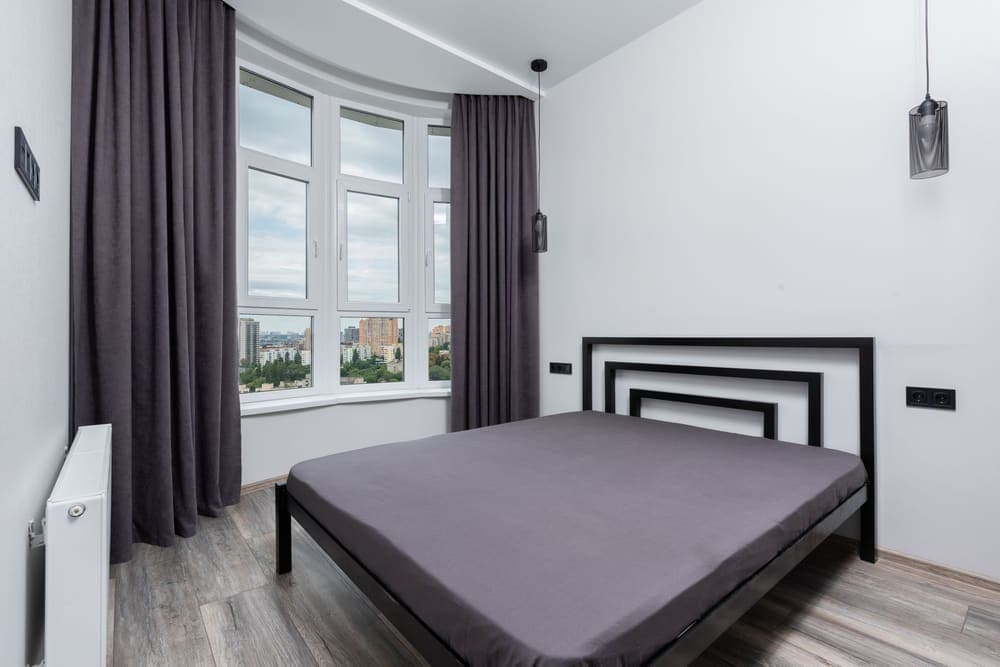 A bed against a wall of pleated floor-length curtains in a dim bedroom