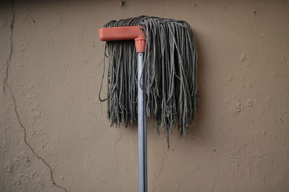 A damp mop leaning against a rough plaster wall