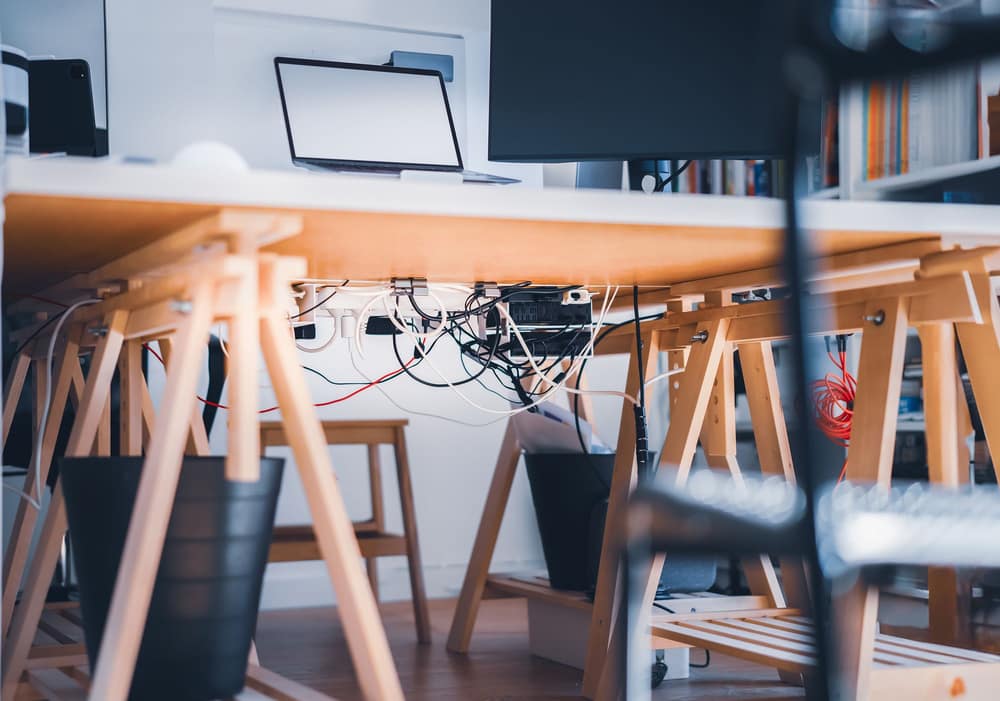 A tangle of cables and power strips under a desk, seen from floor level