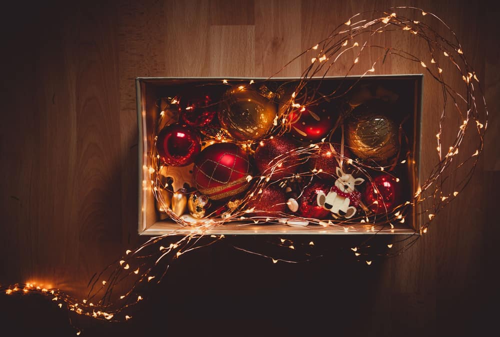 Red and gold Christmas baubles packed into a wooden box with string lights draped over it