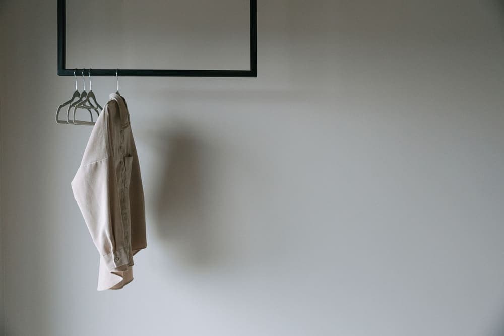 A jacket hanging on a slim freestanding metal clothes rack in a bedroom