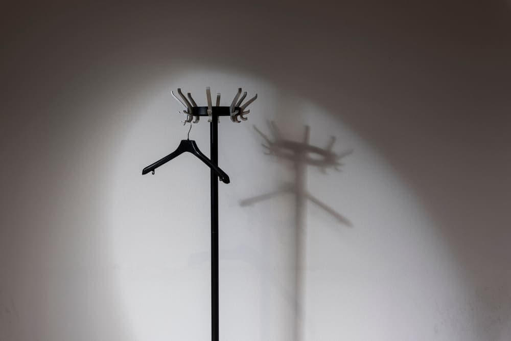 A freestanding coat tree with hooks at the top, casting a shadow on a plain wall