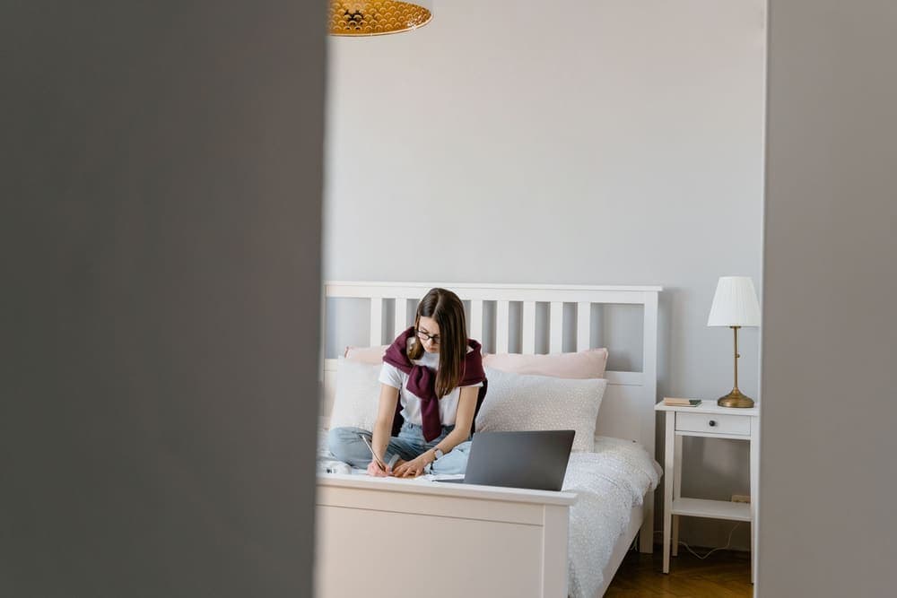 A student working on a bed in a small room