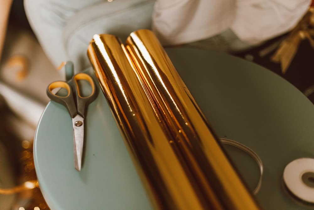 Two rolls of gift wrap on a tray beside scissors and a spool of ribbon