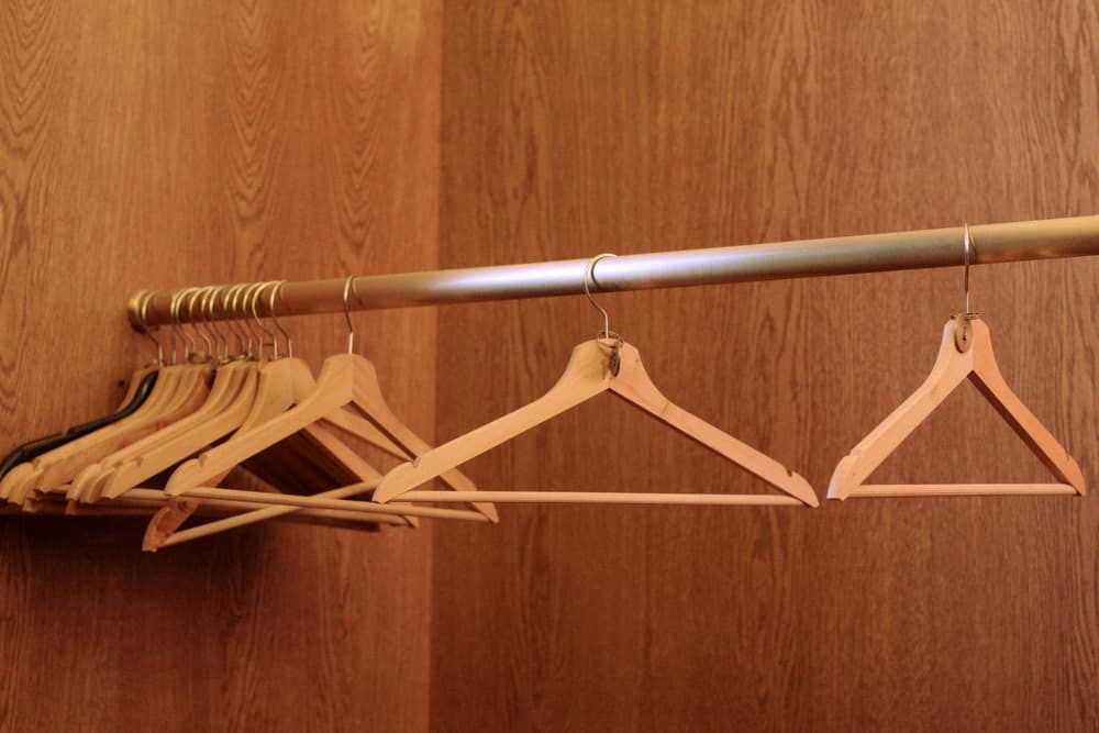 Empty wooden hangers bunched at one end of a closet rod with three spaced out along it