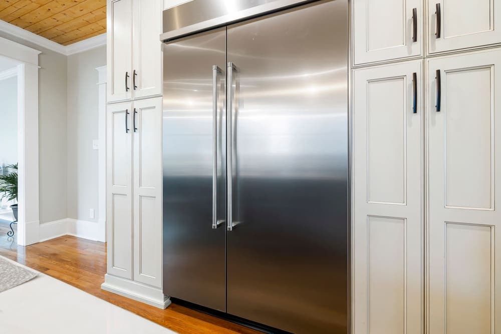 A large stainless steel refrigerator door between white kitchen cabinets