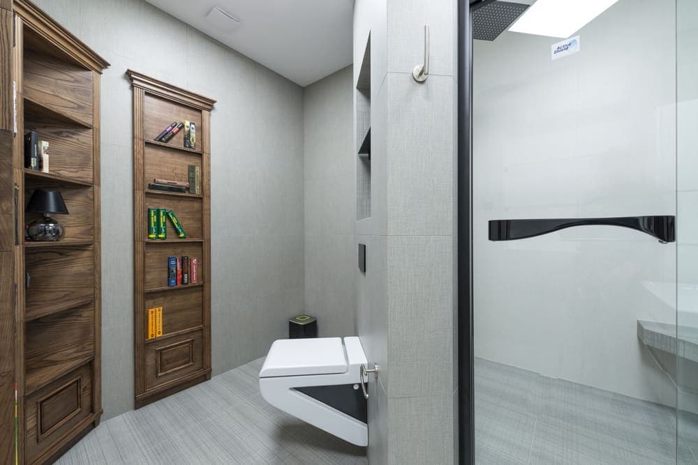 A toilet beside wooden shelving in a light modern bathroom