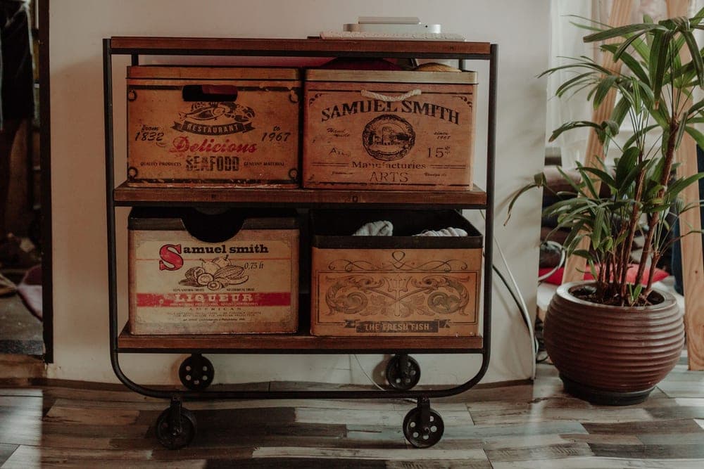 A two-tier metal cart on casters holding wooden crates against an apartment wall