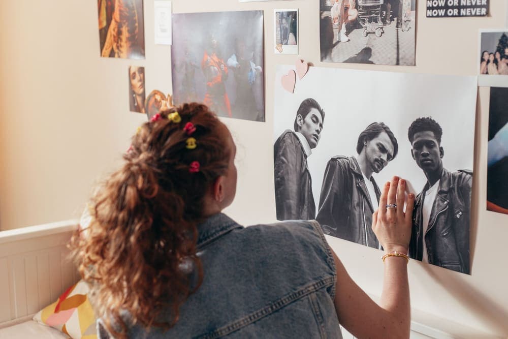 Someone pressing a poster onto a bedroom wall covered with prints and photos