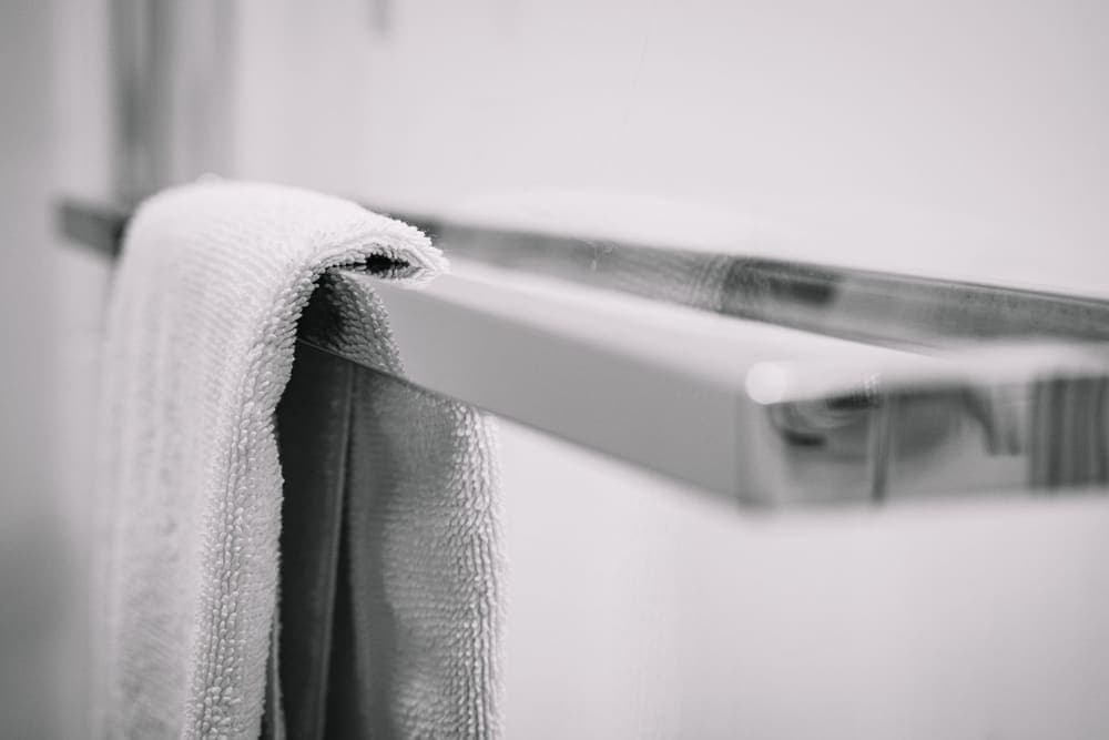 A white towel folded over a chrome towel bar on a pale bathroom wall