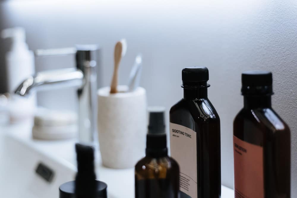 Tall skincare bottles and a toothbrush cup on a bathroom counter beside a basin