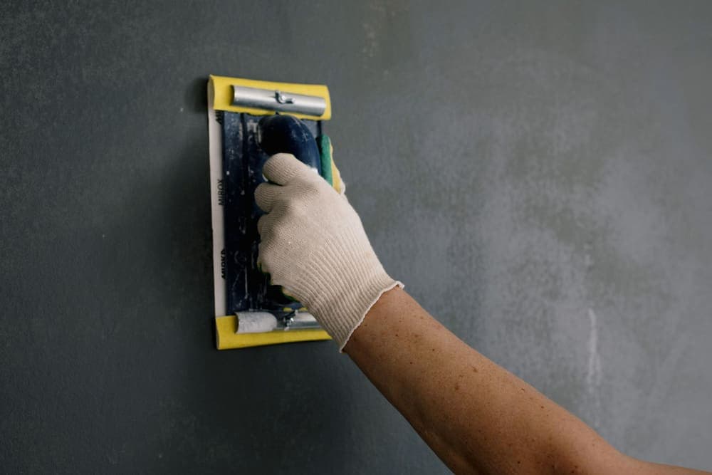 A gloved hand smoothing a patched section of wall with a hand float