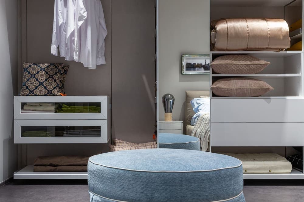 An open wardrobe with hanging clothes and folded bedding on shelves